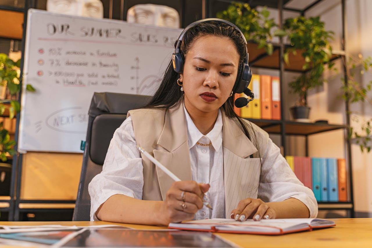 Professional woman wearing a headset taking notes in an office setting, focused on work.